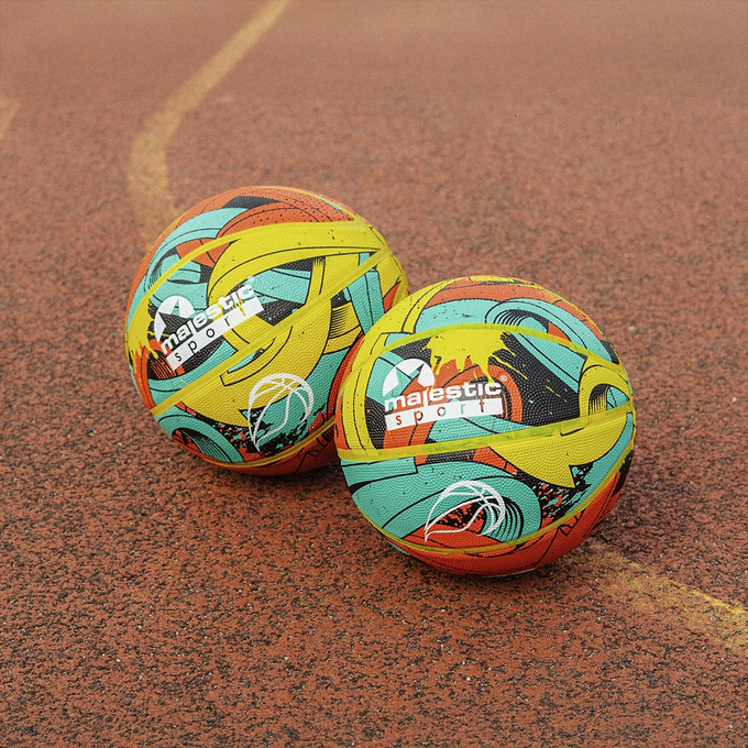 Dwie piłki do koszykówki, Majestic Sport Arrow multicolor, obok siebie na pomarańczowym boisku