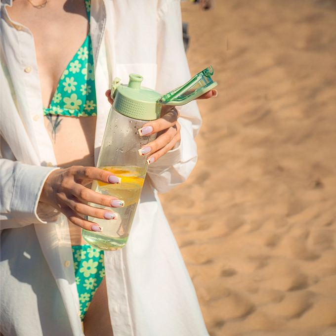 Kobieta trzyma zieloną butelkę tritanową na wodę w dłoni, Majestic Sport Okosei Clear, o pojemności 750ml