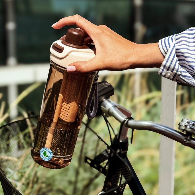 Kobieta wkłada do koszyka rowerowego kawową butelkę tritanową na wodę elementami w dłoni, Majestic Sport Zoya