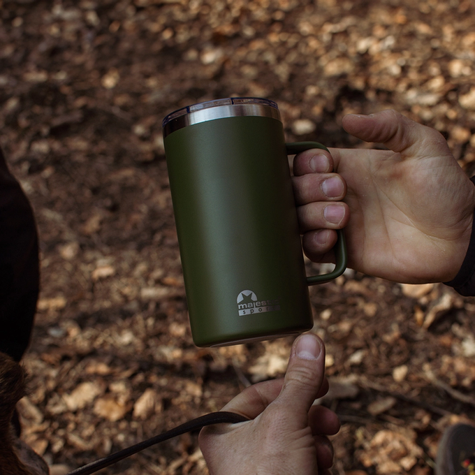 Mężczyzna trzyma w dłoni zielony kubek termiczny z uchwytem, Majestic Sport Gump, idealny na ciepły napój