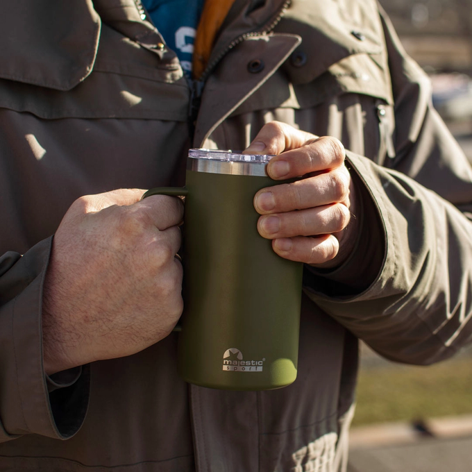 Mężczyzna trzyma w dłoni zielony kubek termiczny z uchwytem, Majestic Sport Gump, idealny na ciepły napój